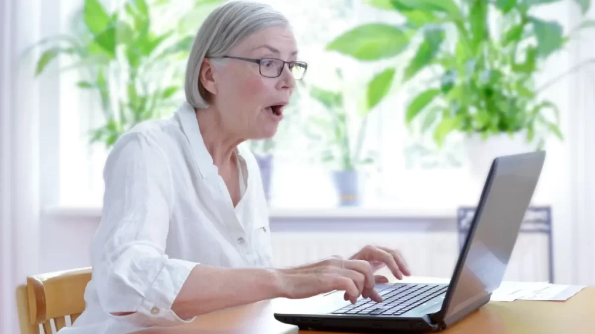 Starší žena v bílé halence vyděčení zírá na notebook