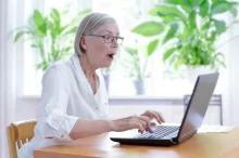 Starší žena v bílé halence vyděčení zírá na notebook