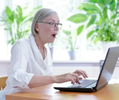 Starší žena v bílé halence vyděčení zírá na notebook