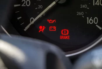 Detail palubní desky automobilu s několika rozsvícenými výstražnými kontrolkami.