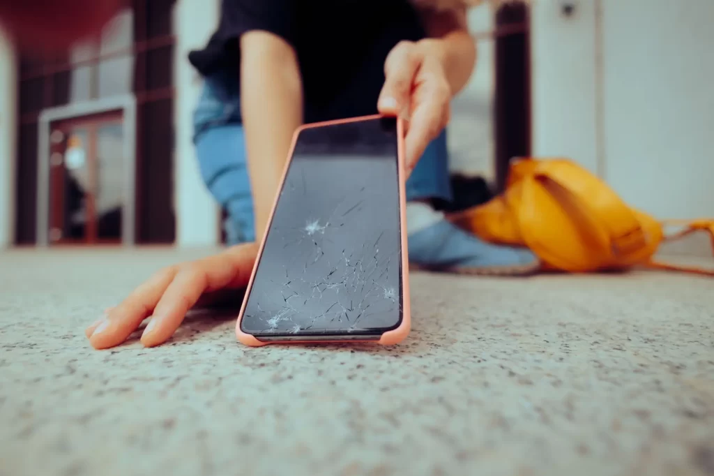 mobil2 - Techsvět Člověk zvedá mobilní telefon s prasklým displejem ze země.
