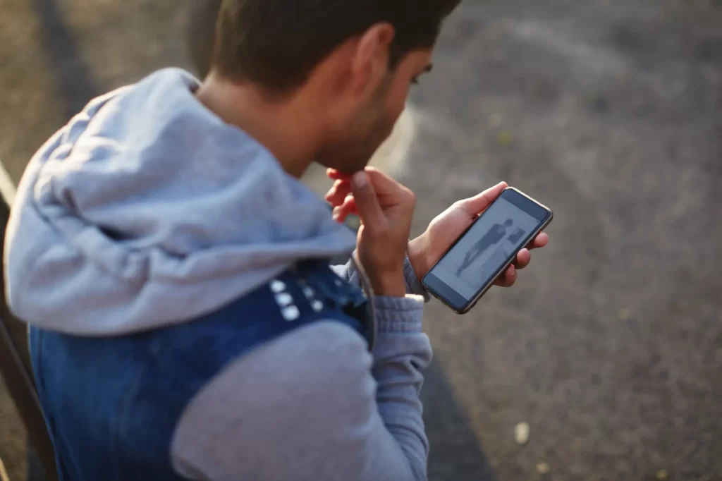 mobil2 - Techsvět Mladý muž sedí venku, drží smartphone v ruce a zaujatě sleduje obsah na displeji.