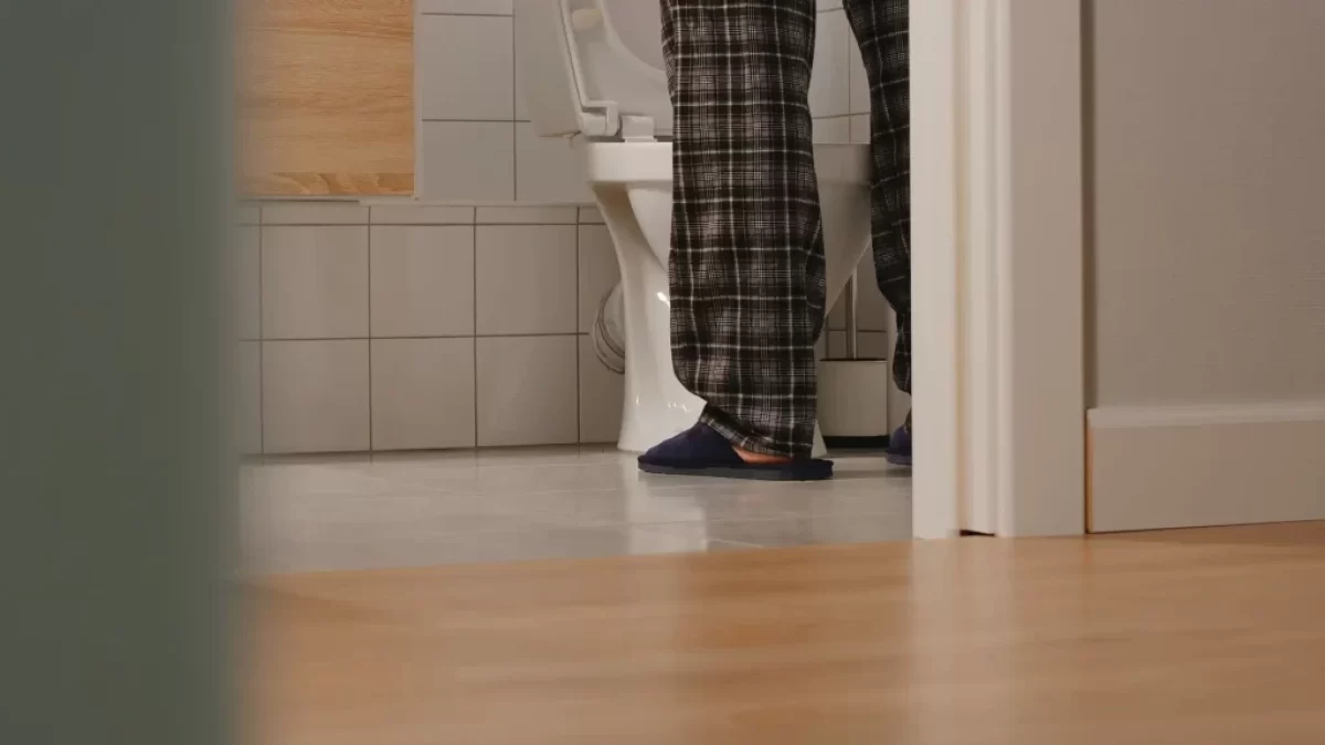 Muž v domácím oblečení a pantoflích stojí u toalety.