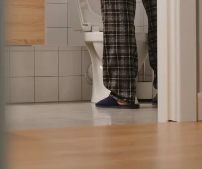 Muž v domácím oblečení a pantoflích stojí u toalety.
