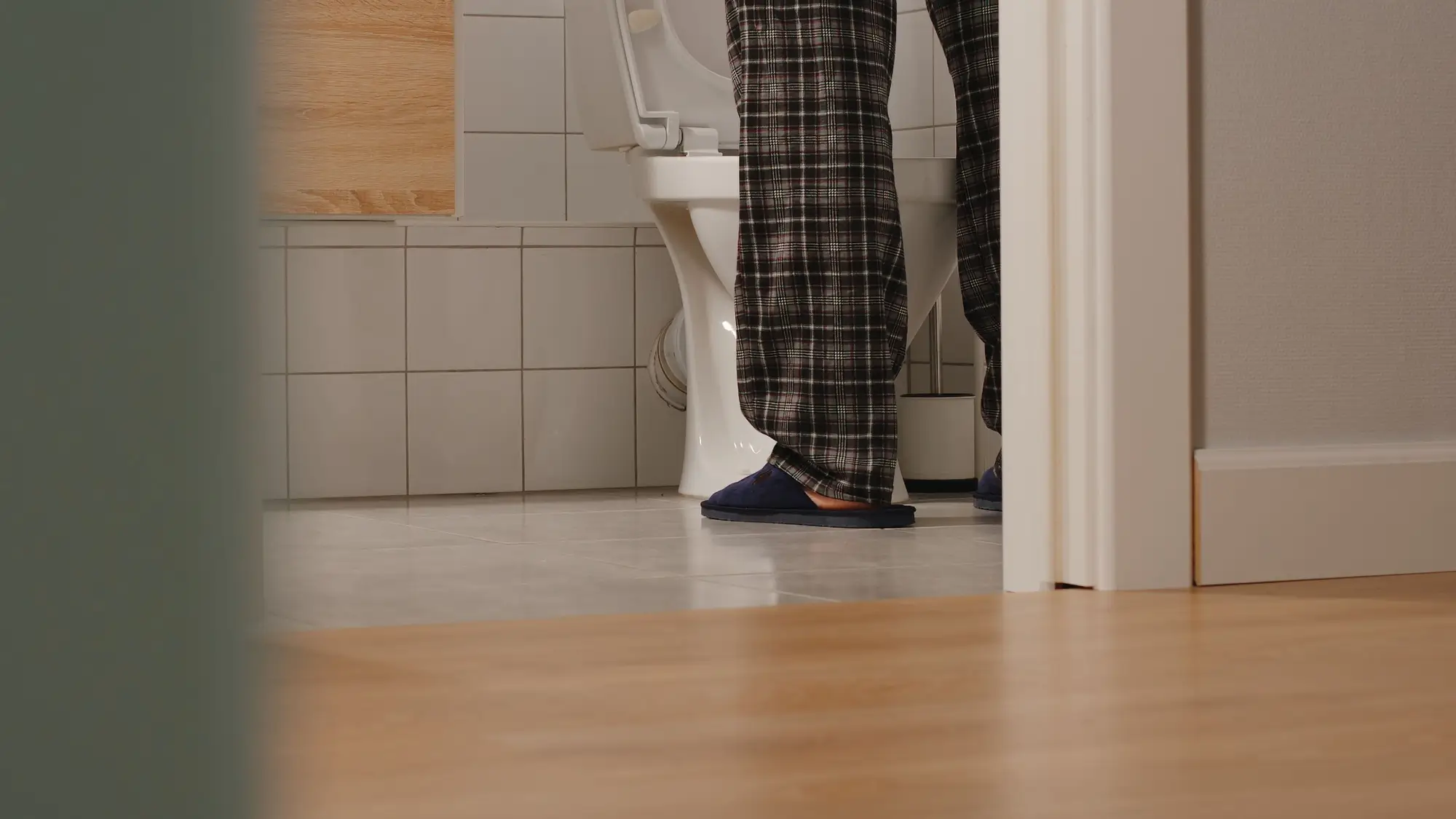 Muž v domácím oblečení a pantoflích stojí u toalety.