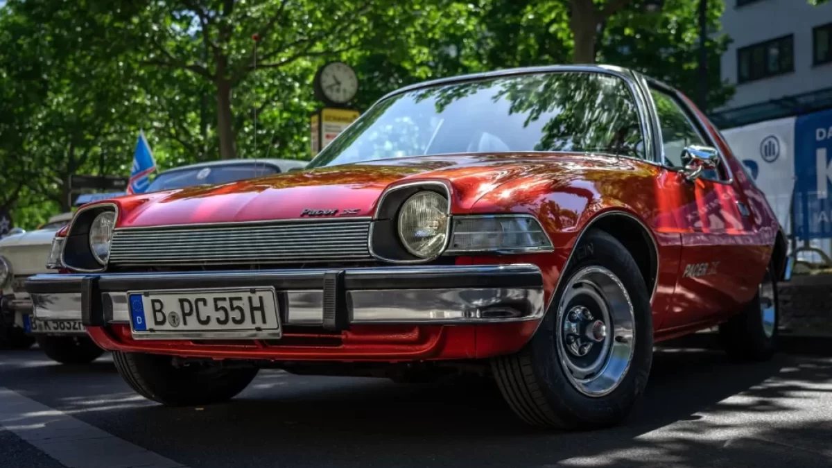 Červený AMC Pacer, zaparkovaný venku pod stromem