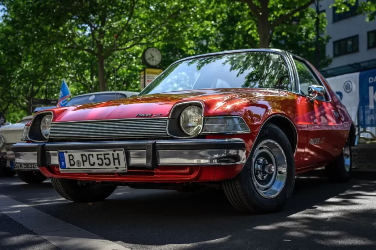 Červený AMC Pacer, zaparkovaný venku pod stromem