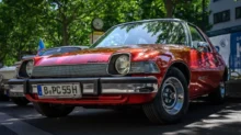 Červený AMC Pacer, zaparkovaný venku pod stromem