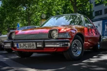 Červený AMC Pacer, zaparkovaný venku pod stromem