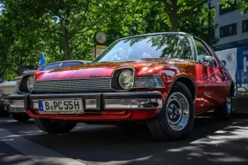 Červený AMC Pacer, zaparkovaný venku pod stromem