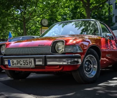 Červený AMC Pacer, zaparkovaný venku pod stromem