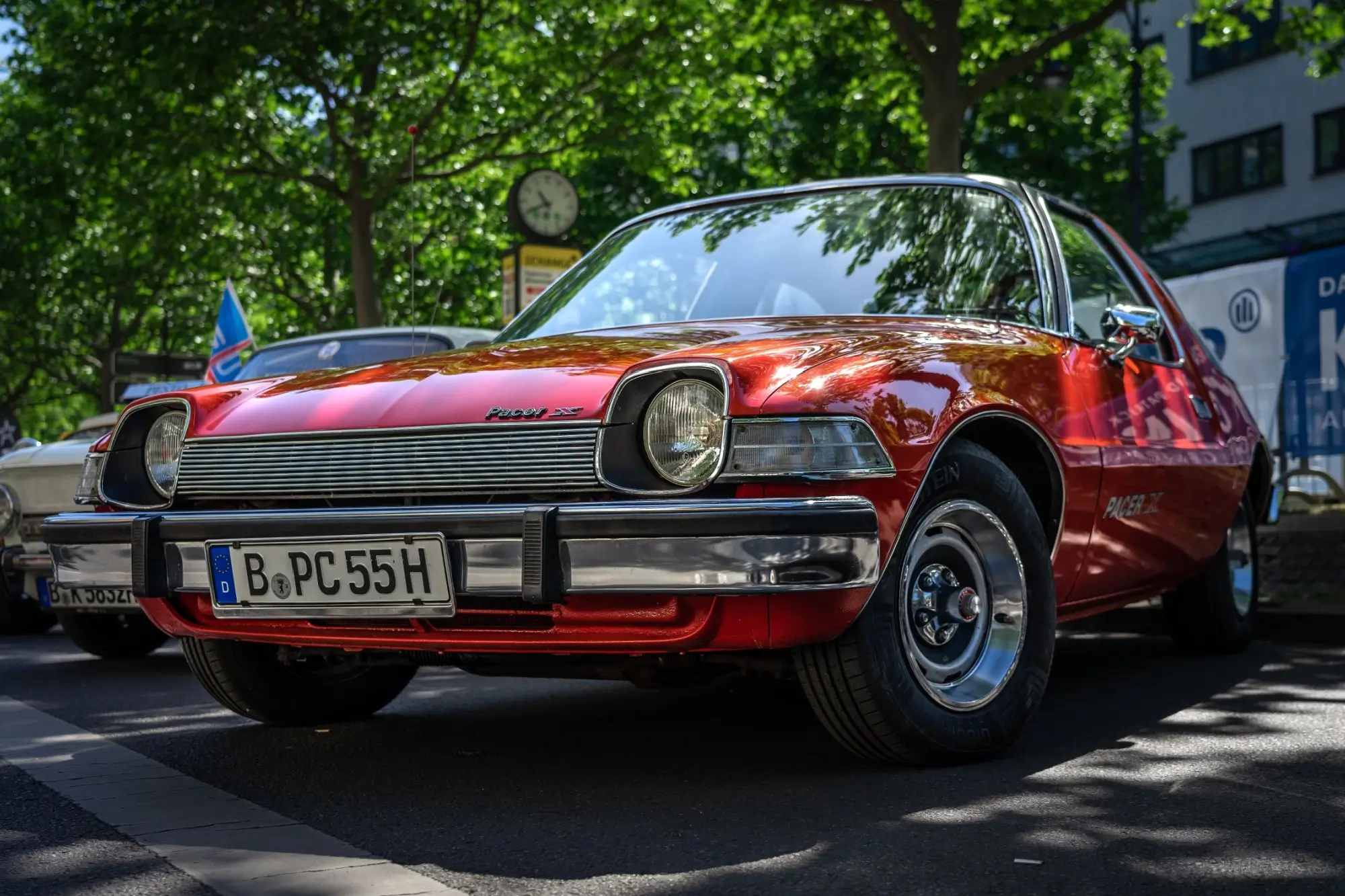 Červený AMC Pacer, zaparkovaný venku pod stromem