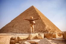 Muž s rozpaženýma rukama před monumentální Cheopsovou pyramidou v Gíze.