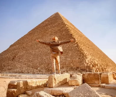 Muž s rozpaženýma rukama před monumentální Cheopsovou pyramidou v Gíze.