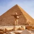 Muž s rozpaženýma rukama před monumentální Cheopsovou pyramidou v Gíze.