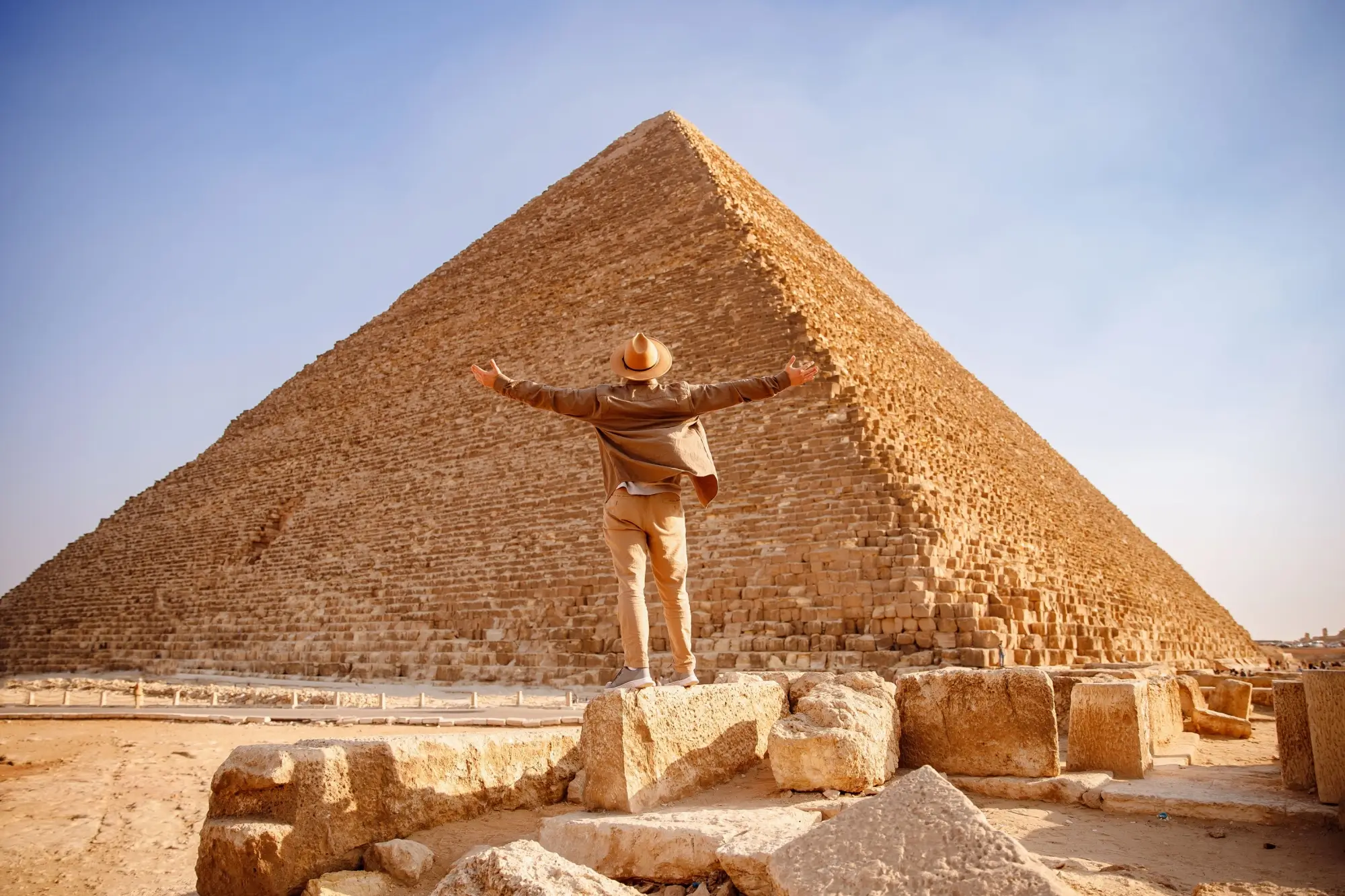 Muž s rozpaženýma rukama před monumentální Cheopsovou pyramidou v Gíze.