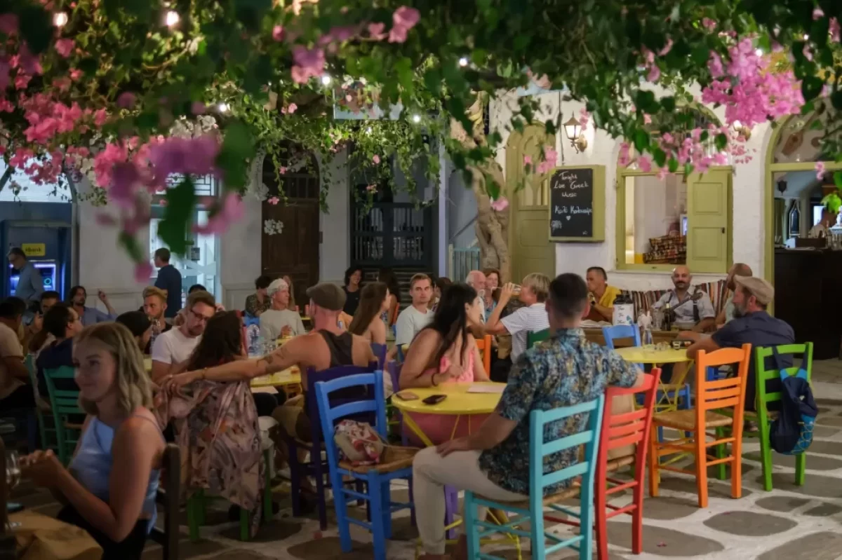 Rušná řecká taverna plná lidí, kteří si užívají večerní atmosféru pod rozkvetlými větvemi.