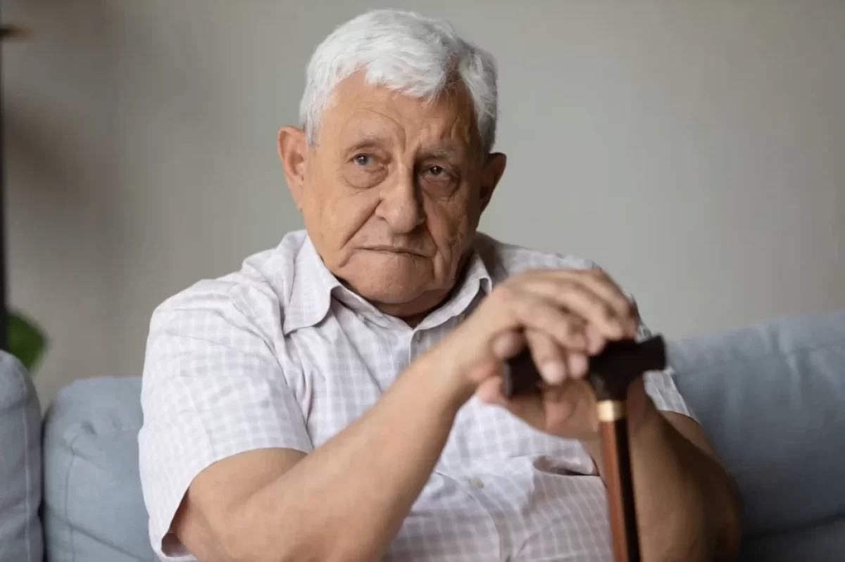 Senior v bílé košili s hůlkou sedí na gauči.