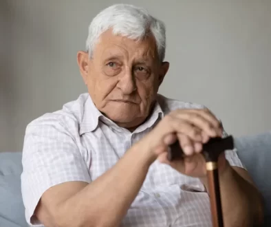 Senior v bílé košili s hůlkou sedí na gauči.