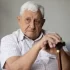 Senior v bílé košili s hůlkou sedí na gauči.