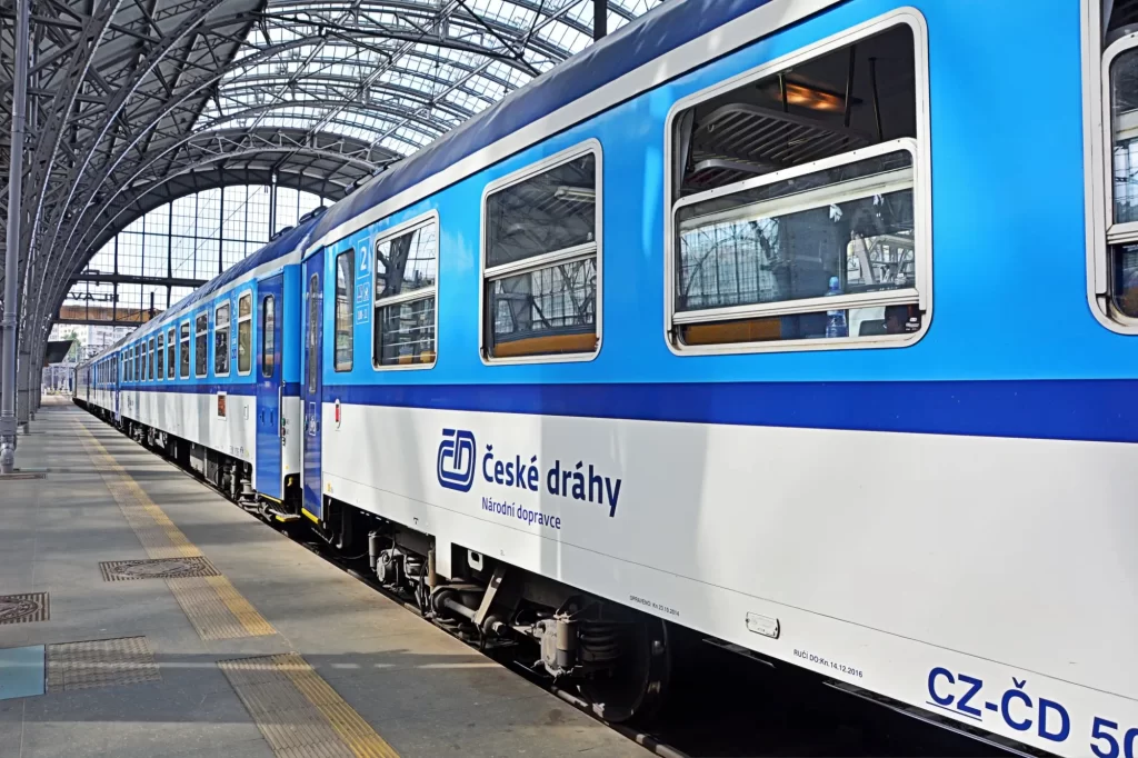 Modrobílý vlak Českých drah stojící u nástupiště ve velké kryté hale hlavního nádraží.