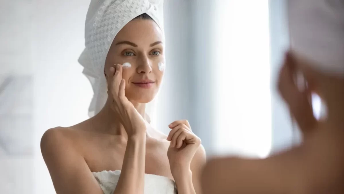 žena před zrcadlem aplikuje krém na tvář