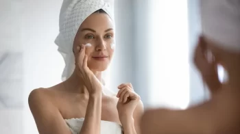 žena před zrcadlem aplikuje krém na tvář