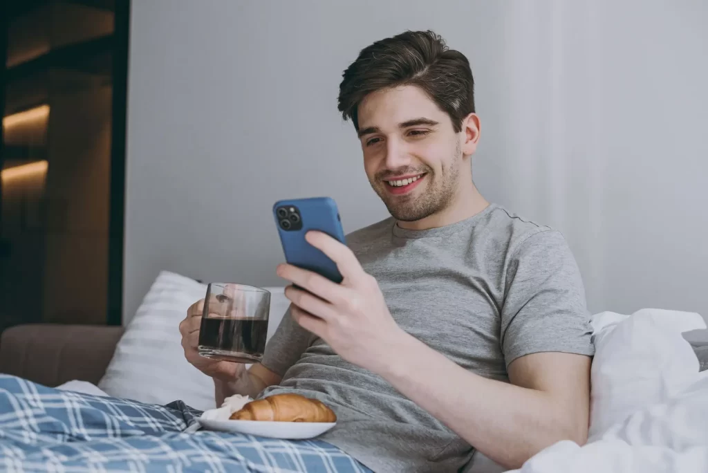 shutterstock_2132902567 - Techsvět muž v posteli snídá a dívá se do telefonu