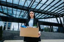 žena opouští kancelářskou budovu s krabicí s osobními věcmi v rukách