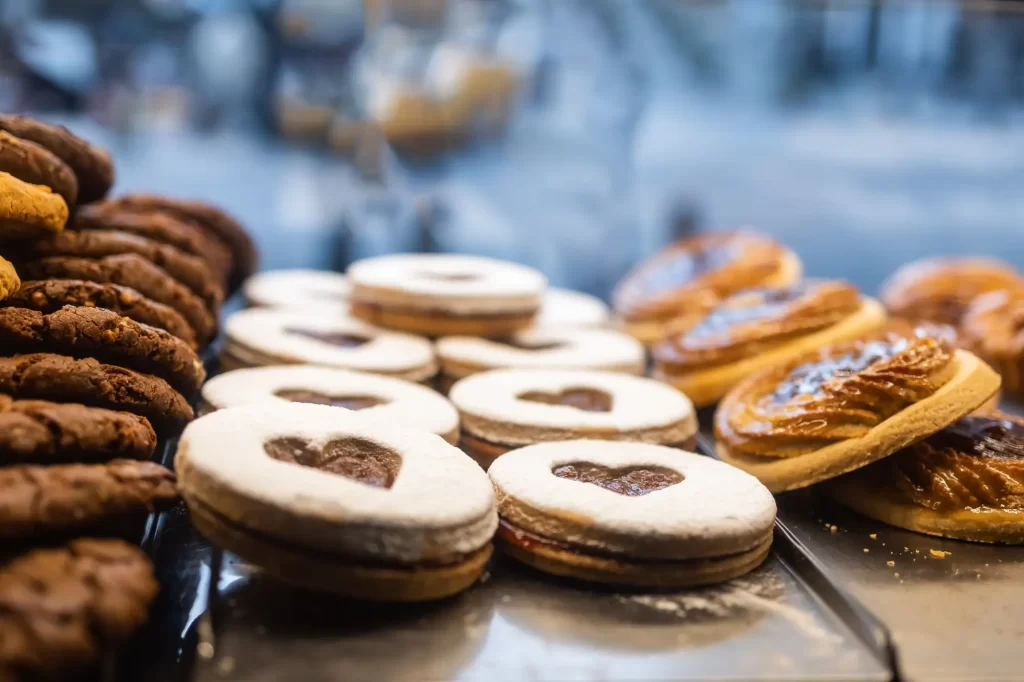 sladké1 - Techsvět Vitrína plná sladkého pečiva a sušenek. V popředí vidíme linecká kolečka s marmeládou ve tvaru srdce, vedle nich jsou čokoládové cookies.