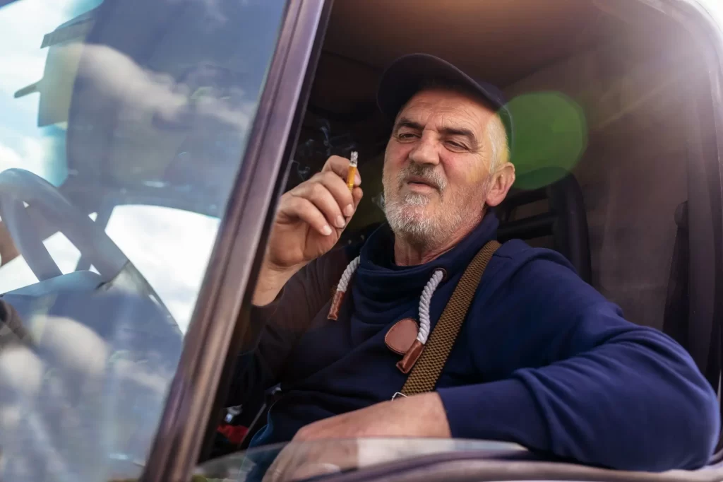 test2 - Techsvět Starší muž sedící za volantem nákladního vozidla, opírající se o okénko a držící cigaretu.