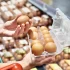 Žena v obchodě drží otevřenou plastovou krabičku s deseti hnědými vejci.
