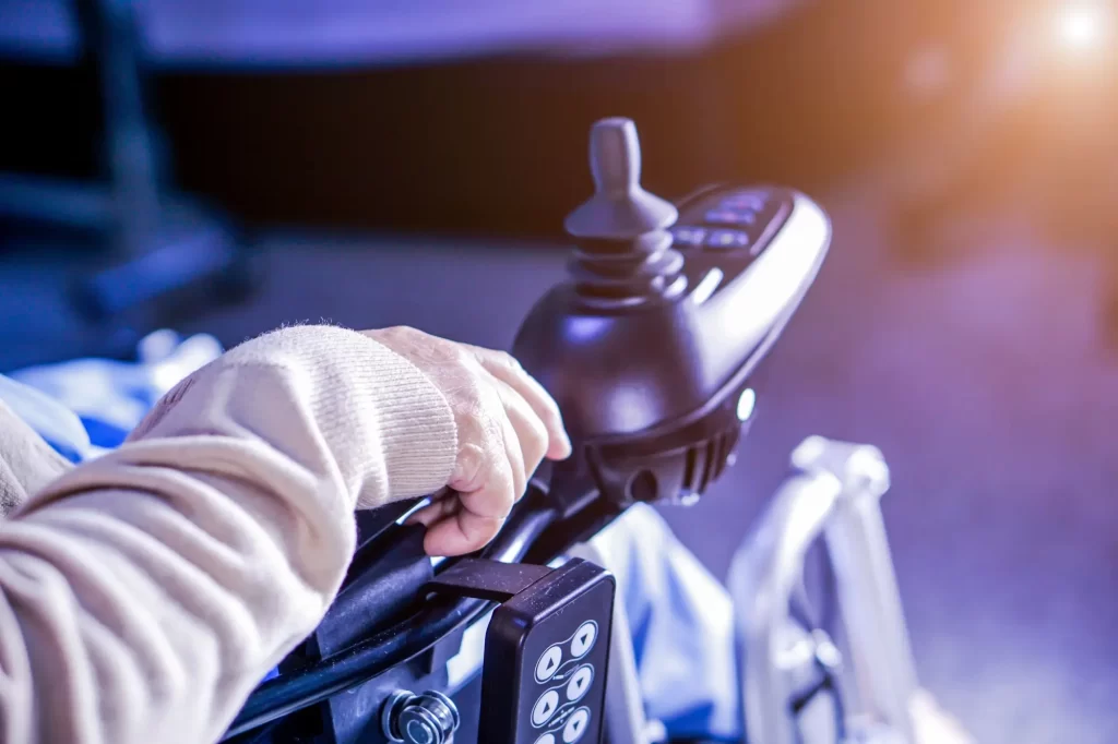 vozík2 - Techsvět Detailní pohled na ruku seniora, která ovládá joystick elektrického invalidního vozíku.