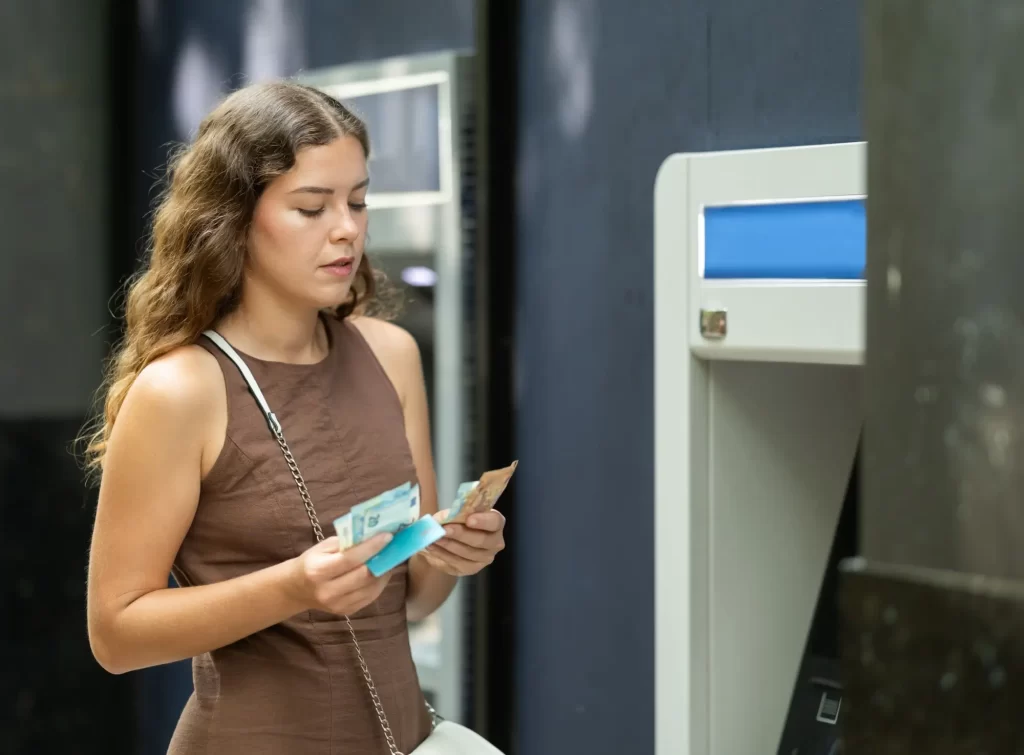 bank2 - Techsvět Mladá žena stojí před bankomatem a počítá právě vybrané bankovky.
