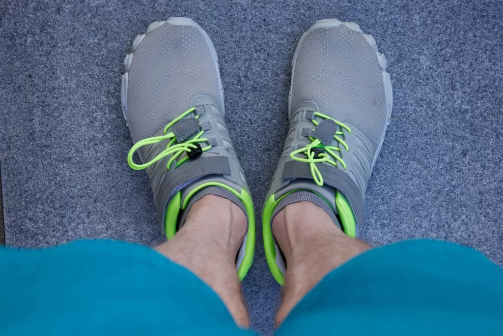 bare3 - Techsvět Obuté nohy v moderních barefoot botách. Boty jsou šedé s výraznými limetkově zelenými detaily a šněrováním.