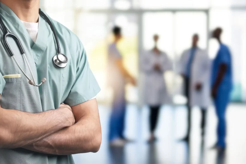 doktor3 - Techsvět Záběr na lékaře v zeleném pracovním oděvu se založenýma rukama a fonendoskopem kolem krku.