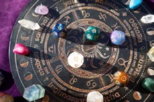 Detailní záběr na astrologický kruh se symboly zvěrokruhu a osmihranné kostky s astrologickými a planetárními znaky.