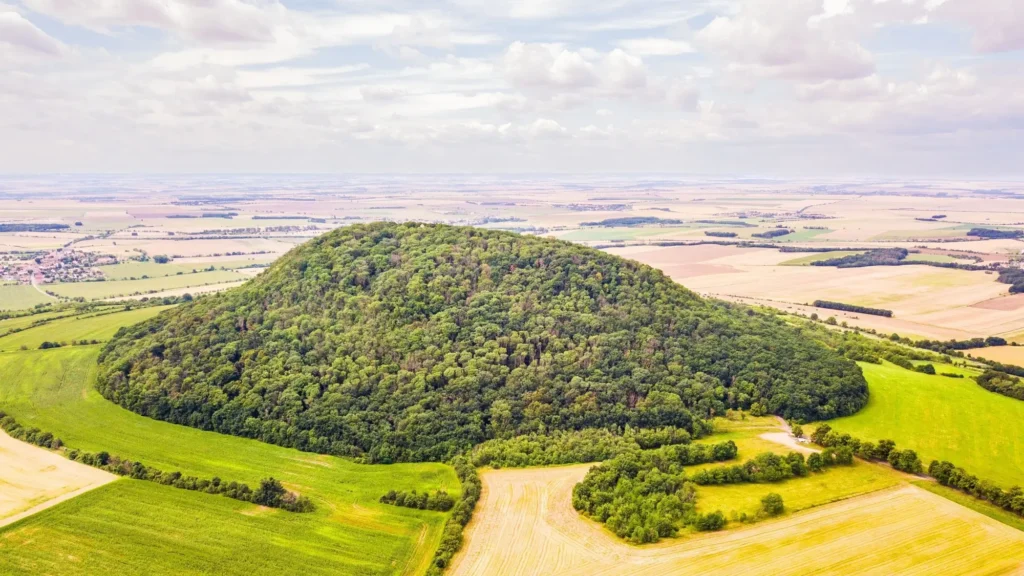 k2 - Techsvět Letecký pohled na zalesněný vrch uprostřed nížiny, obklopený zemědělskou krajinou.