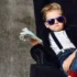 Chlapec sedí na křesle ve slunečních brýlích a balíkem peněz v ruce