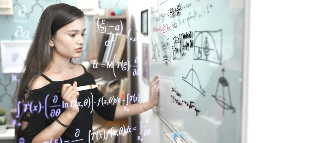 Mladá žena s dlouhými tmavými vlasy, která píše fixem na skleněnou tabuli plnou matematických vzorců, grafů a rovnic. 