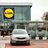 Vstup do prodejny Lidl s výrazným logem na moderní prosklené budově.