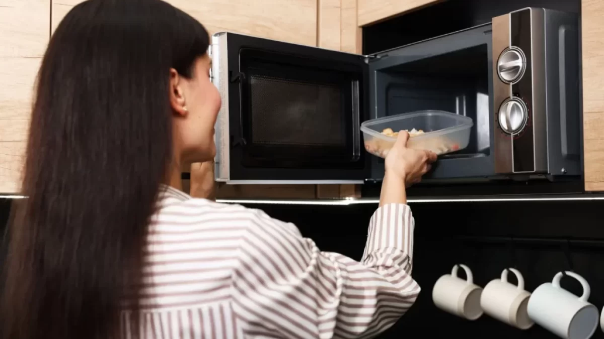 Žena vkládá plastovou misku s jídlem dop mikrovlné trouby