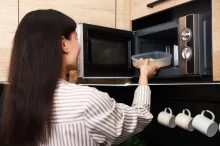 Žena vkládá plastovou misku s jídlem dop mikrovlné trouby