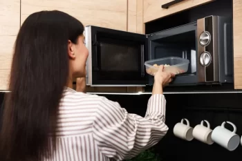 Žena vkládá plastovou misku s jídlem dop mikrovlné trouby