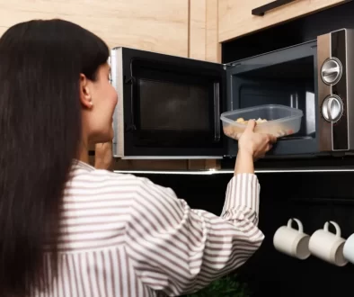 Žena vkládá plastovou misku s jídlem dop mikrovlné trouby