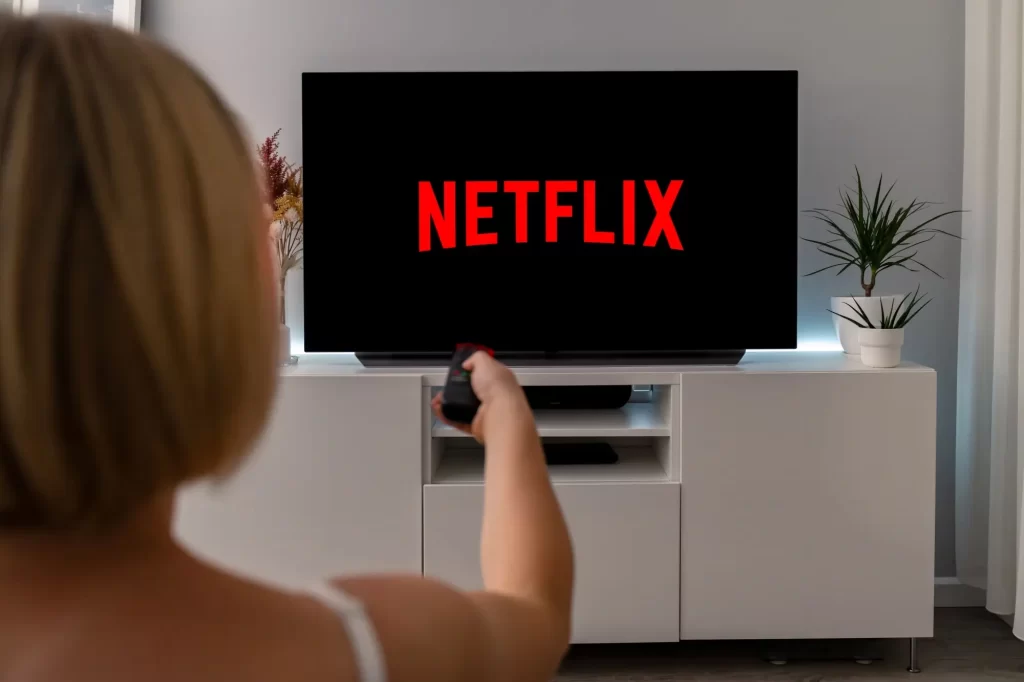 netflix2 - Techsvět Žena sledující televizi, na jejíž obrazovce svítí červené logo Netflixu.