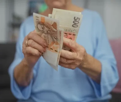 Starší žena v modré halence, která si doma prohlíží nebo přepočítává české bankovky.