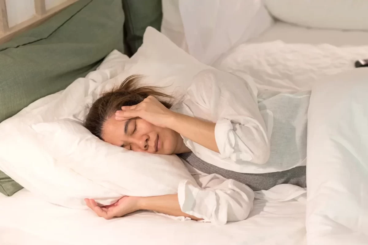 žena leží v posteli s bolestí hlavy