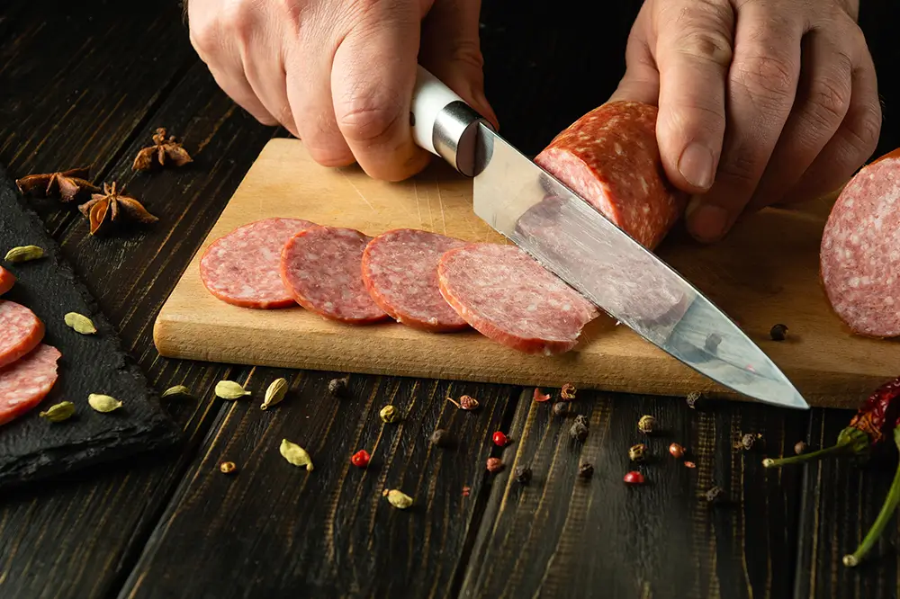 Vysoký obsah nasycených tuků v levných uzeninách přispívá k nárůstu hladiny cholesterolu, ateroskleróze a srdečně-cévním chorobám. - Techsvět muž krájí salám