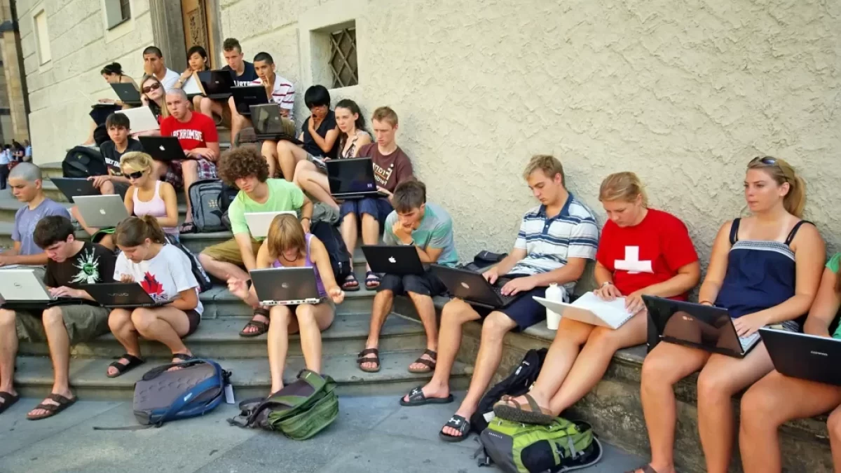 Skupina dětí sedí s notebooky na schodech